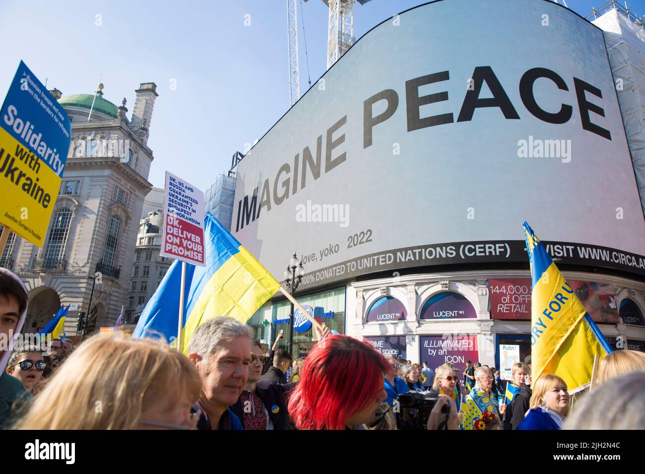 ‘IMAGINE PEACE’, a message by Yoko Ono is displayed on the large electric board as people march during the ‘London Stands with Ukraine' march. Stock Photo