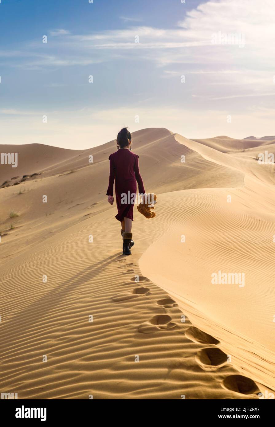 Young girl waking away with a teddy bear in hand in a desert Stock Photo