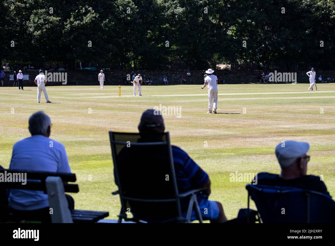 Village Cricket match being watched by interested spectators on a beautiful tree lined ground in mid summer in West Yorkshire Stock Photo