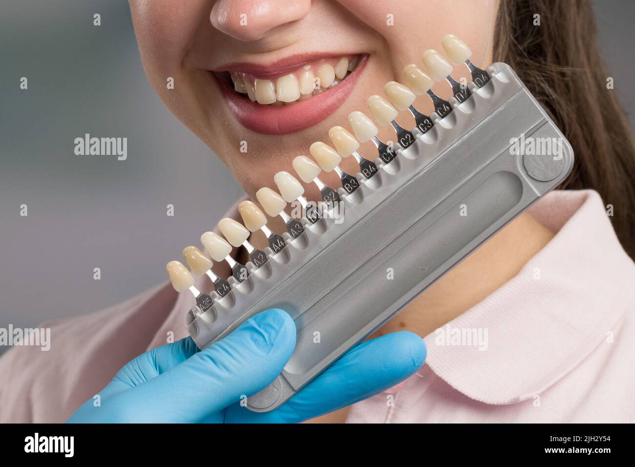 Closeup of dentist using shade guide at woman's mouth to check shade