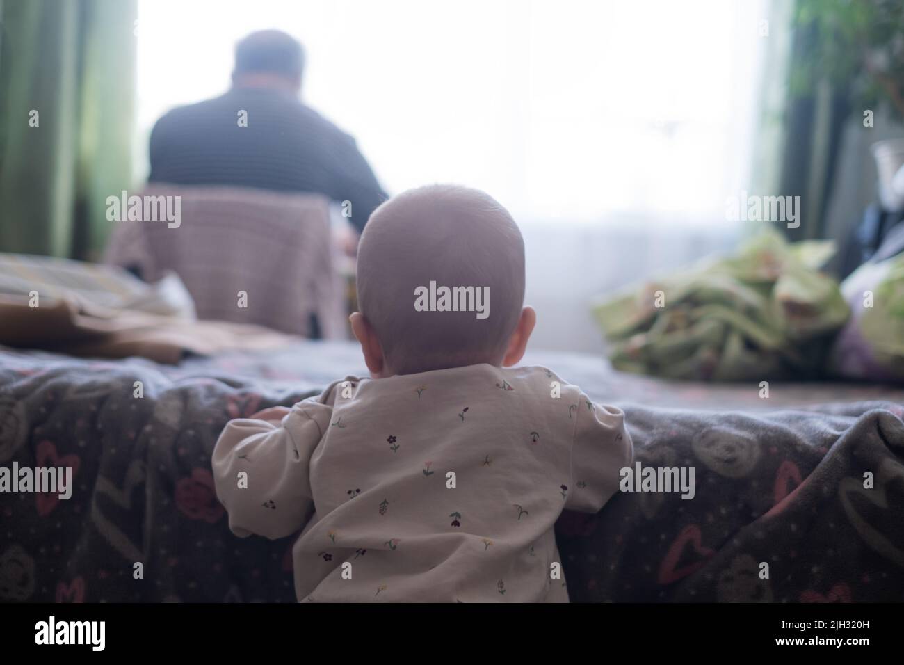 Baby gril looking on her father working at home. Baby want to play with parent Stock Photo