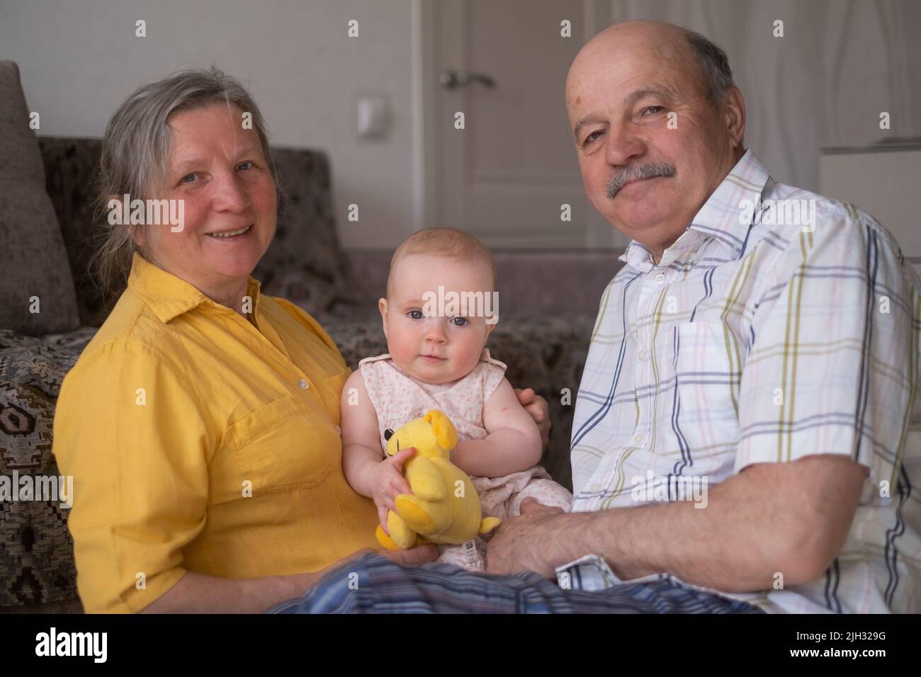 Senior caucasian couple with baby granddaughter posing sitting at home Stock Photo