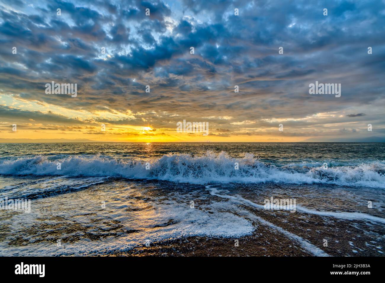 An Ocean Wave Is Breaking Against A Colorful Sunset Sky Stock Photo
