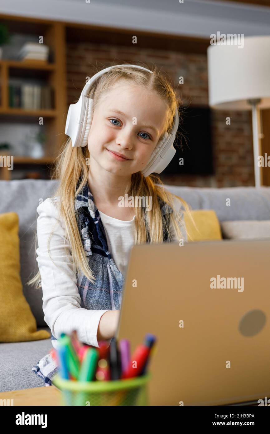 Portrait of cute primary school girl studying at home using laptop ...