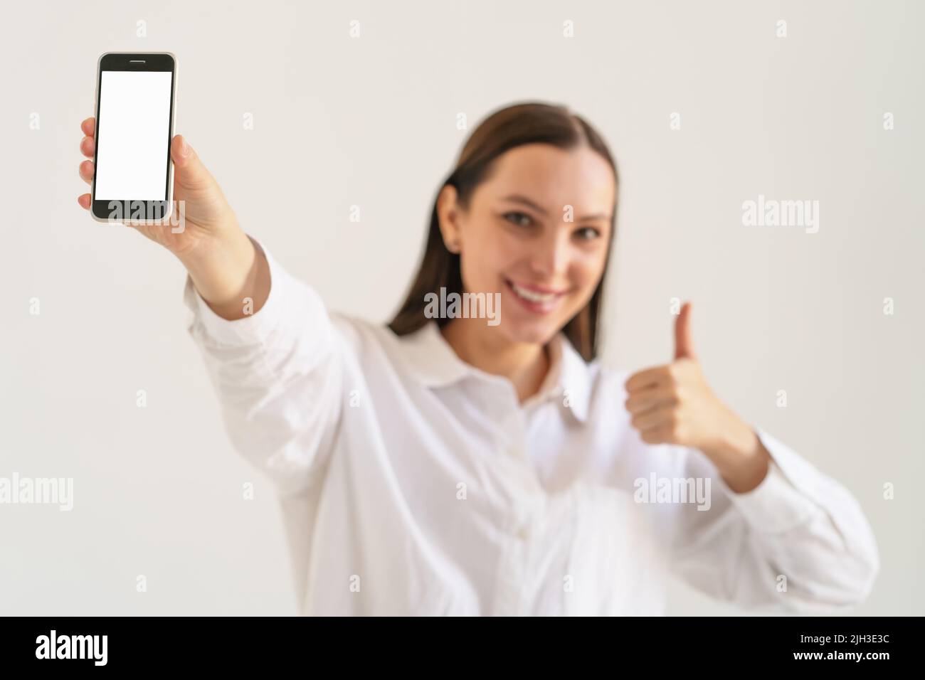 Young brunette woman showing smartphone screen, close up on hand with phone. Mockup image with copy space on display for design. Stock Photo