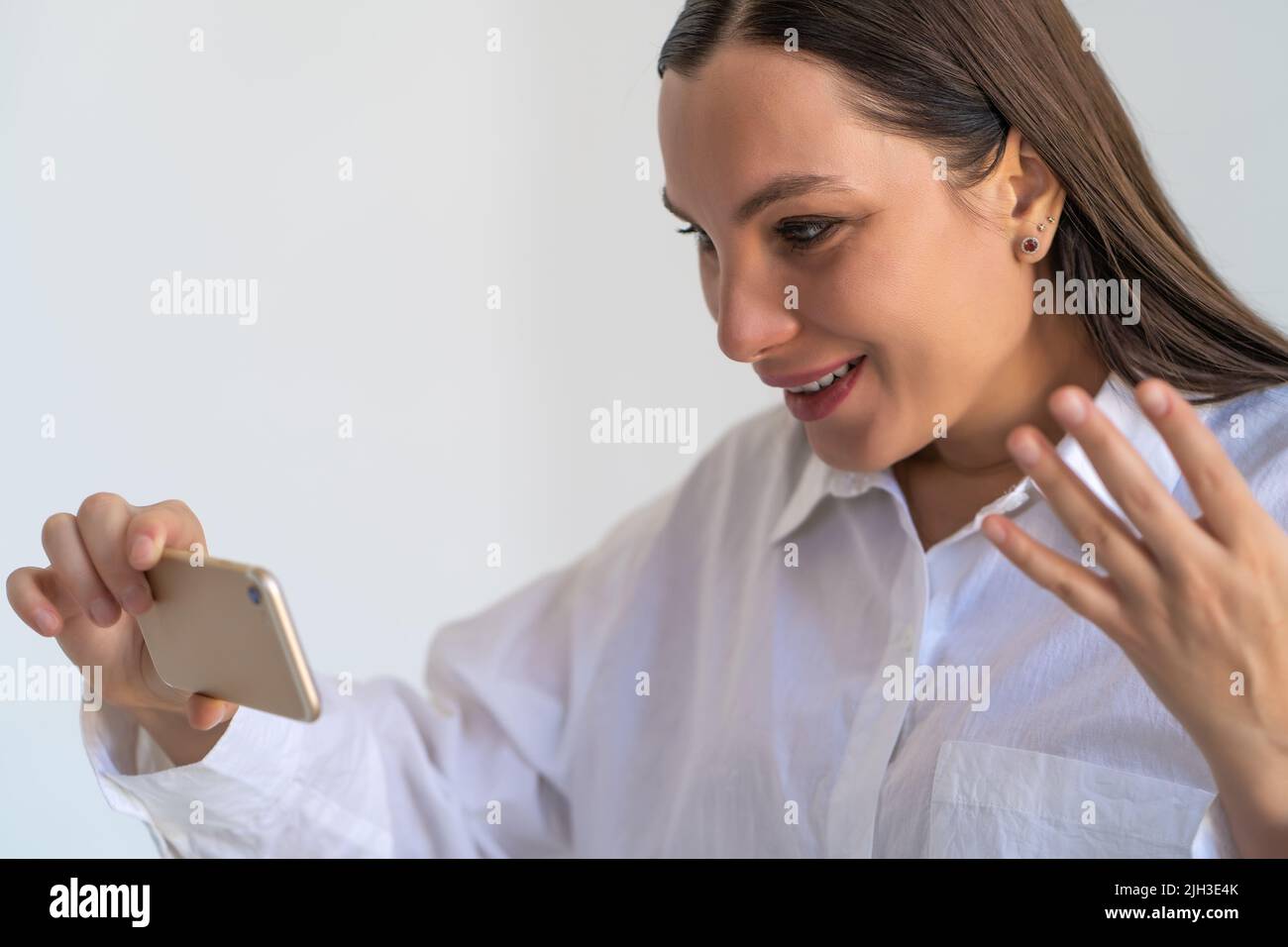 Young brunette woman emotionally talk on video call holding smartphone in hand. Stock Photo