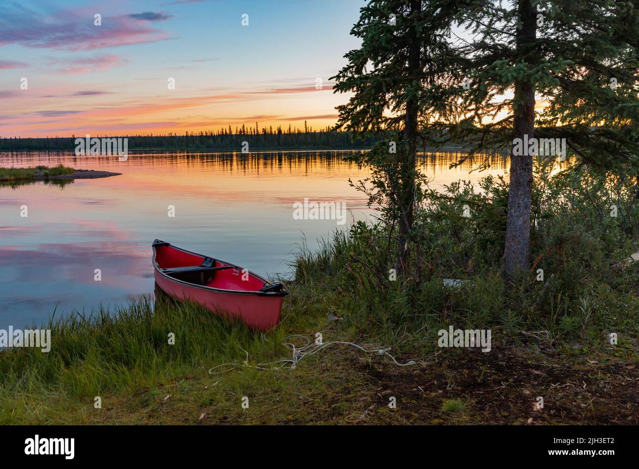 Red canoe parked at cabin  under the summer midnight sun, along shoreline of Great Bear Lake, Northwest Territories, Canada. Stock Photo