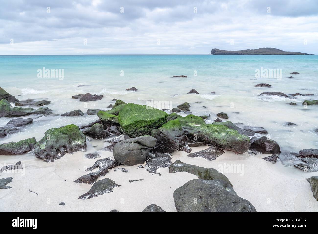 Mossy rocks on beautiful white sand beach and blue waters in the Galapagos Stock Photo