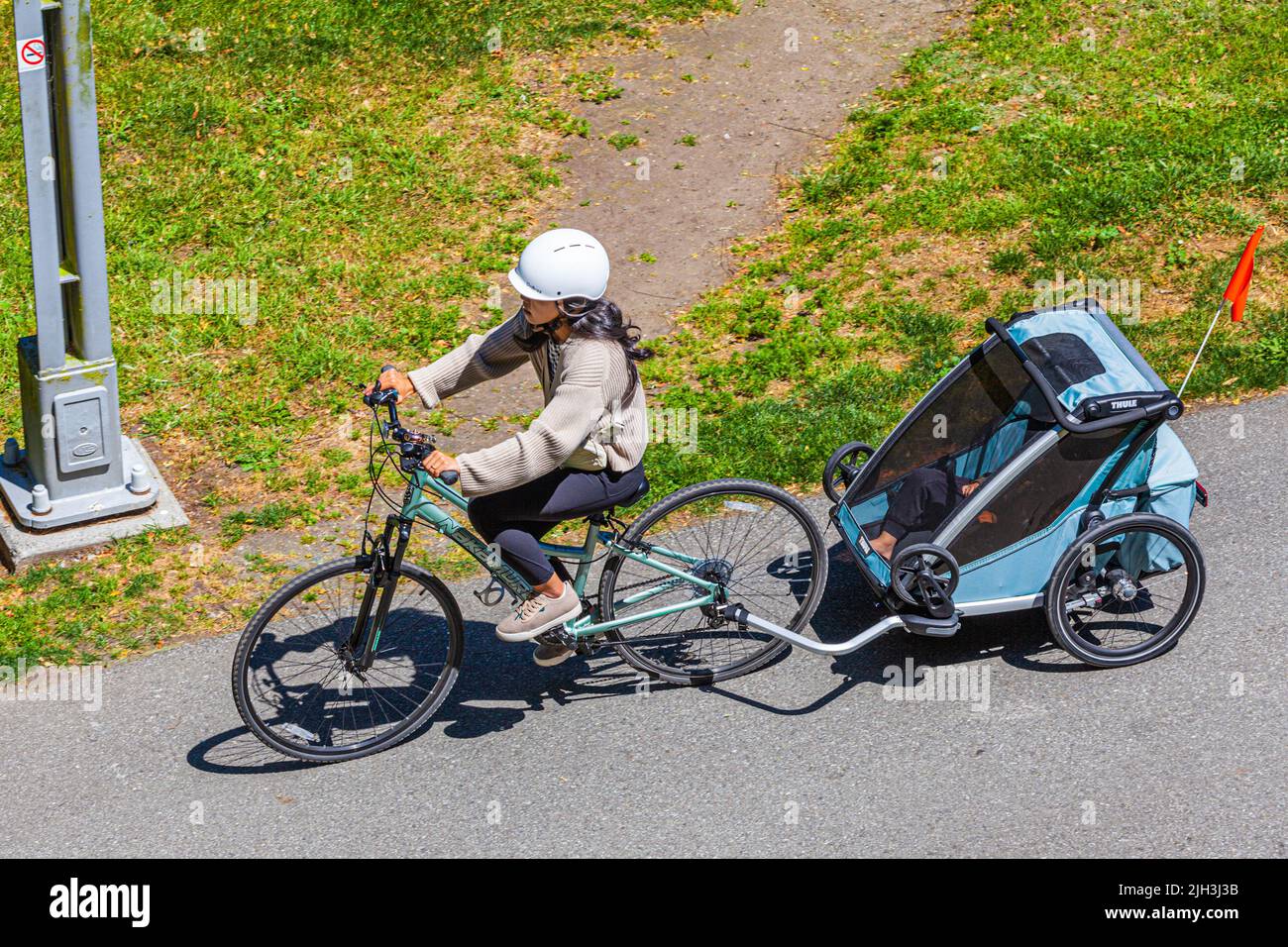 Young mother cycling with her child in a carrier along a bike path in Steveston British Columbia Canada Stock Photo