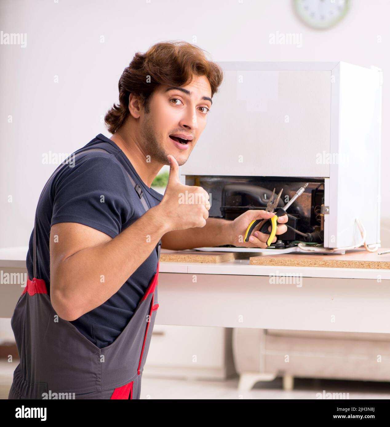 Young handsome contractor repairing fridge Stock Photo