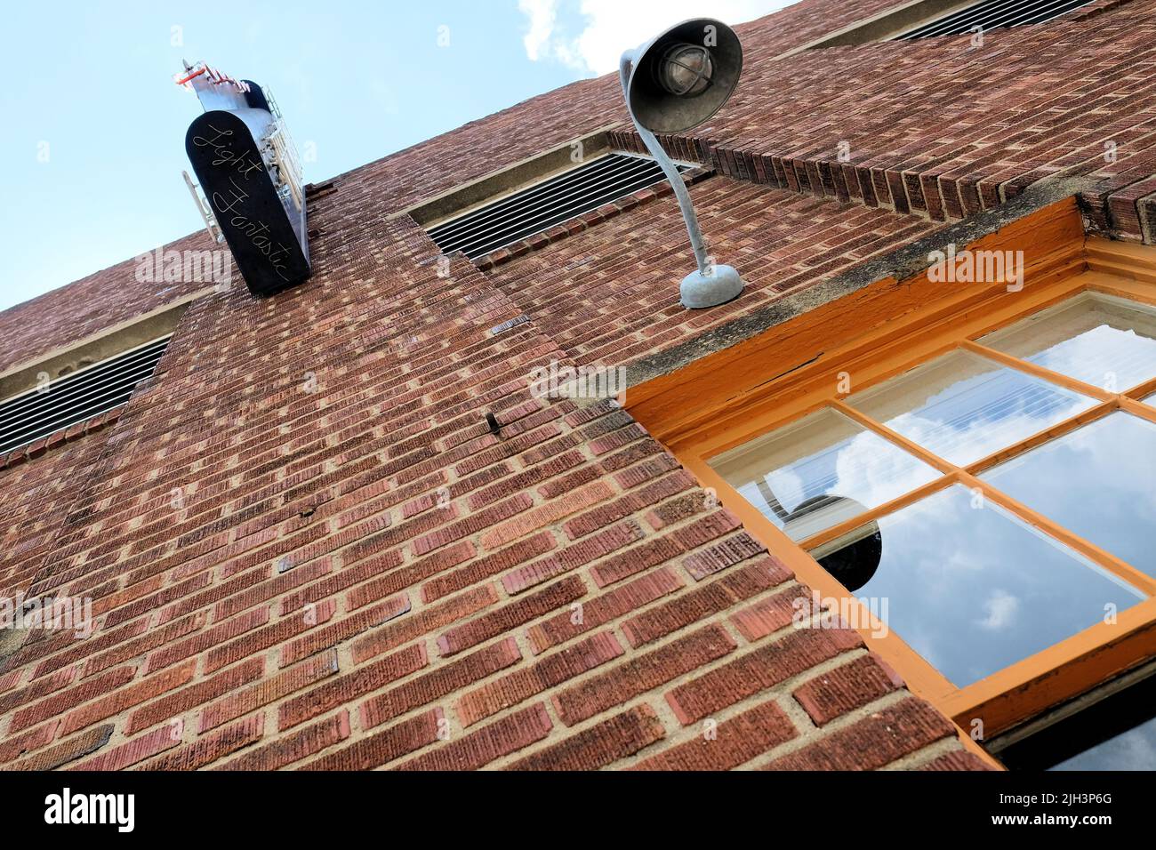 Exterior  brick wall looking up from the street with a window, street lamp and the underside of a neon sign with Light Fantastic signature; Asheville. Stock Photo