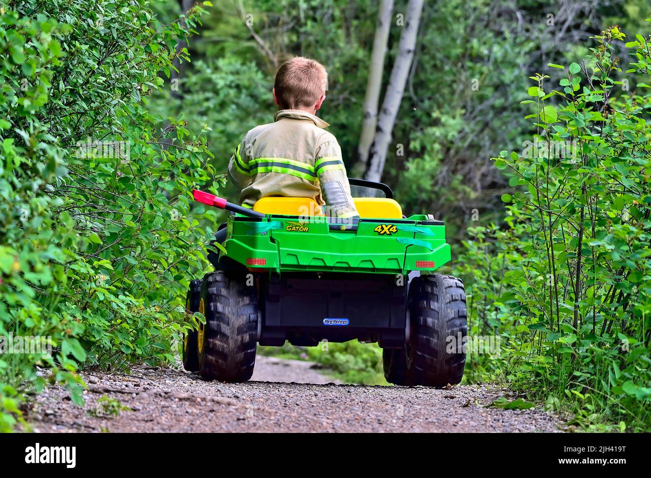 A rear view of a young boy driving his toy 4x4 on a park trail in rural Alberta Canada Stock Photo