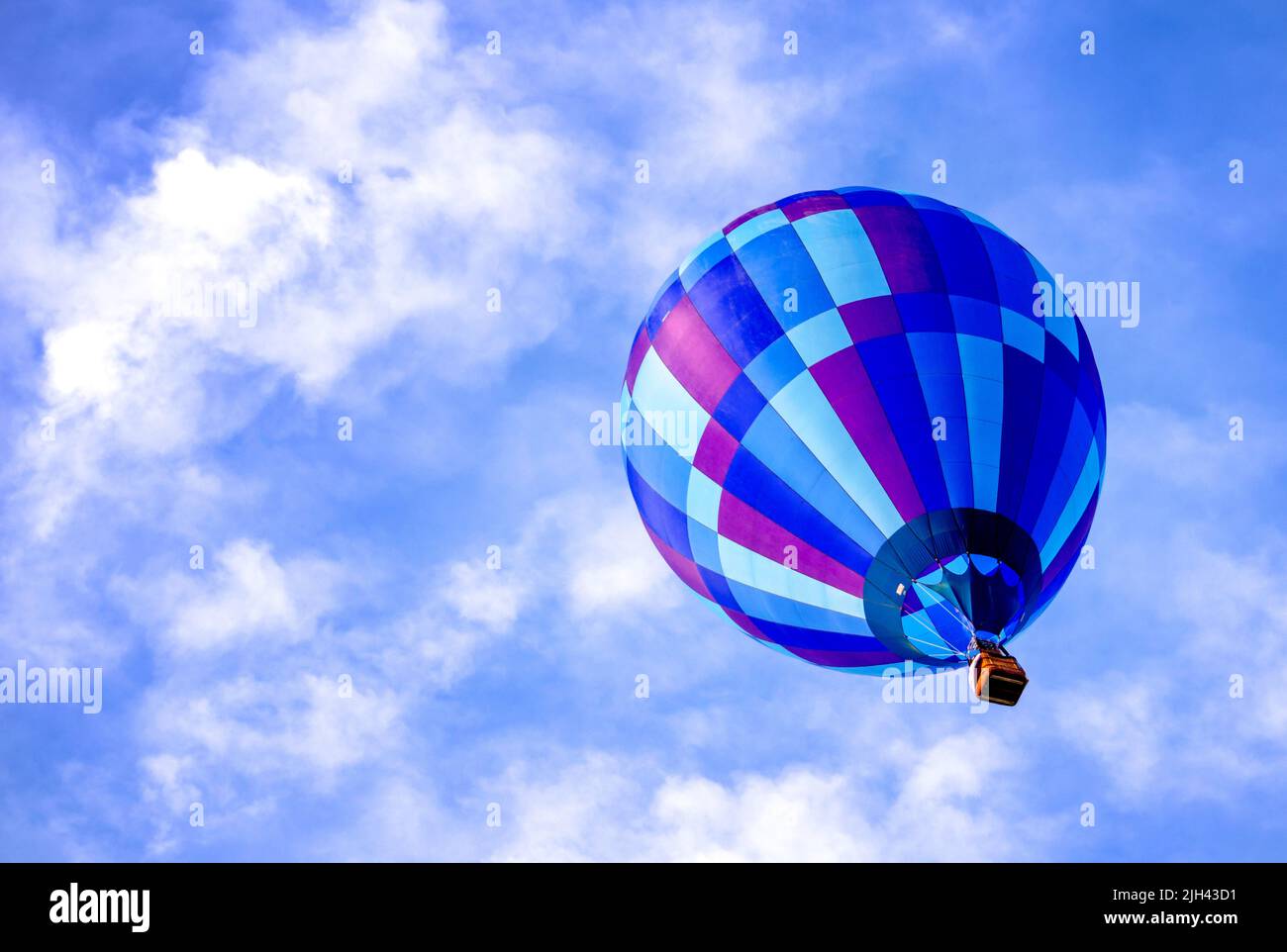 Large blue hot air balloon floats in a cloudy blue sky Stock Photo