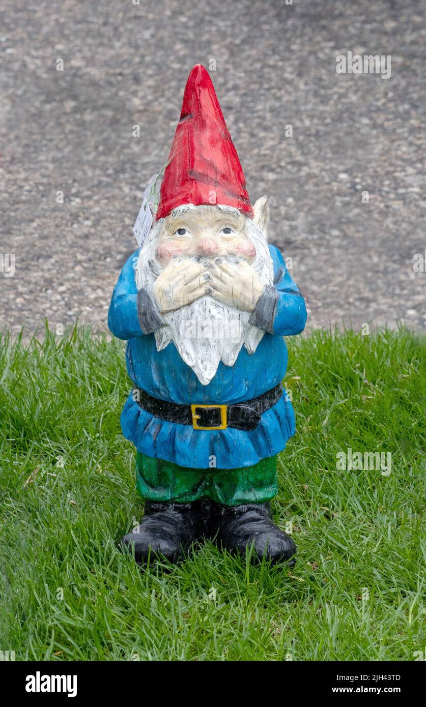 A naughty gnome statue stands in embarrassment with hands over his mouth Stock Photo
