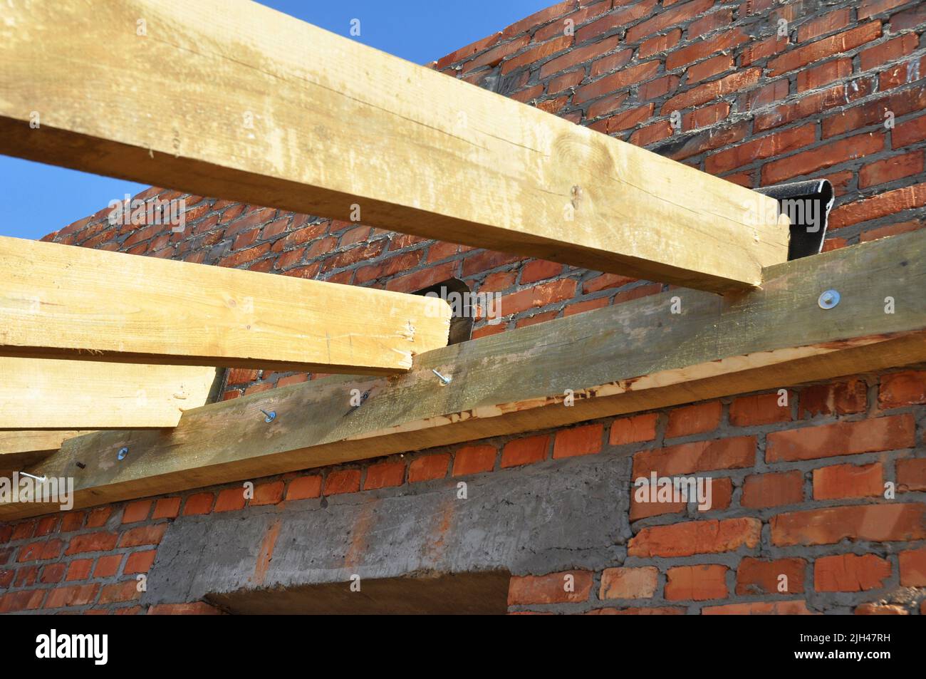 Wooden beams frame roofing construction on brick house wall Stock Photo