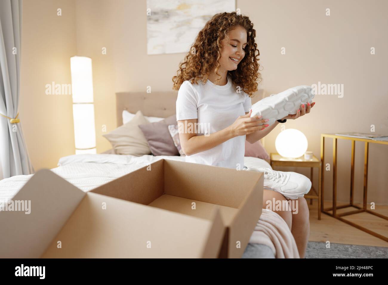 Happy young woman unboxing package in bedroom Stock Photo