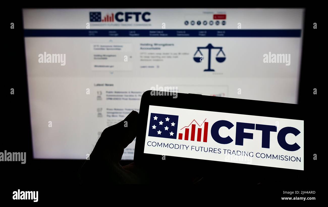 Person holding smartphone with logo of US Commodity Futures Trading Commission (CFTC) on screen in front of website. Focus on phone display. Stock Photo