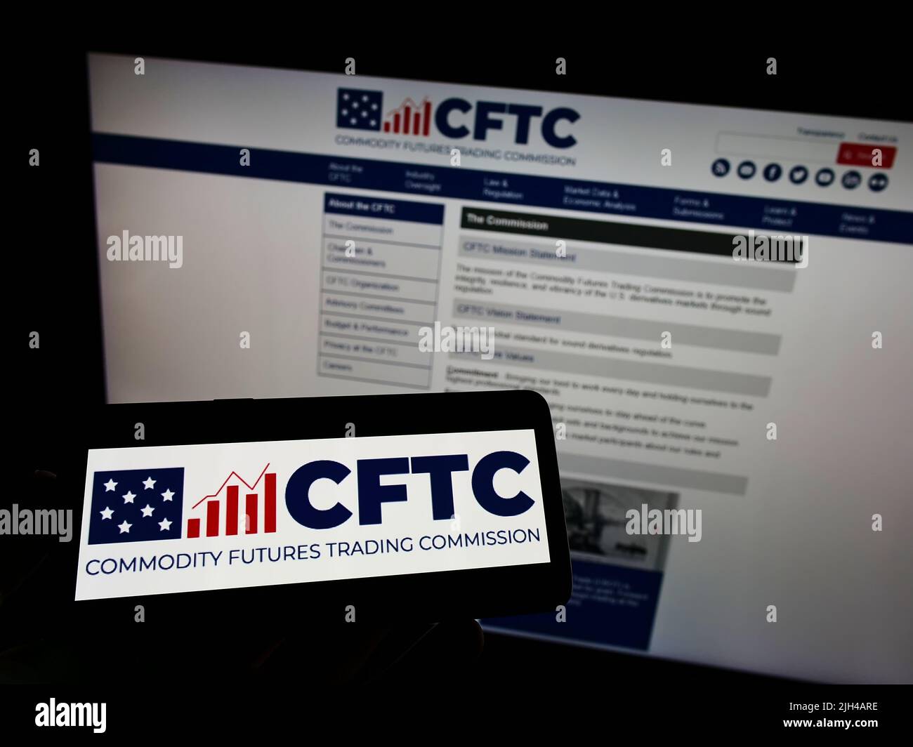 Person holding mobile phone with logo of US Commodity Futures Trading Commission (CFTC) on screen in front of web page. Focus on phone display. Stock Photo