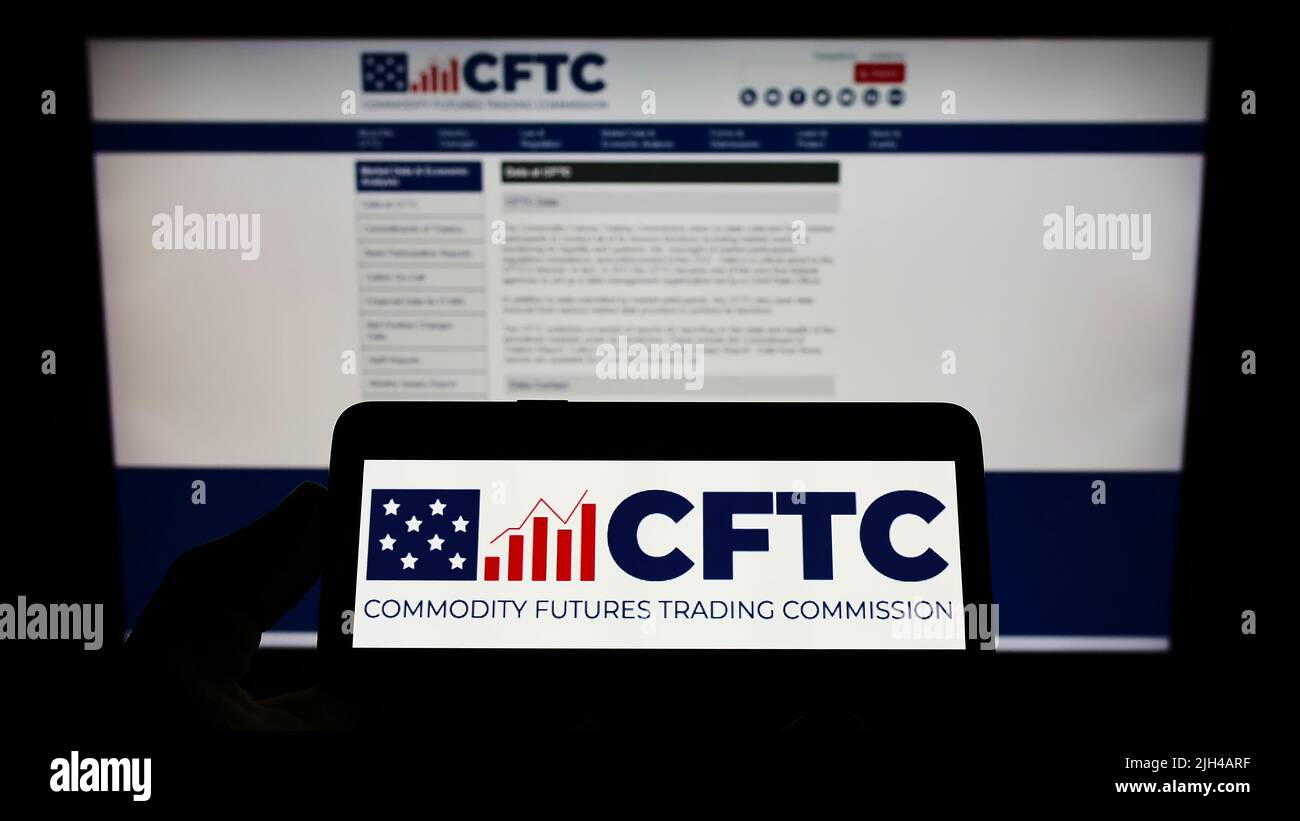 Person holding cellphone with logo of American Commodity Futures Trading Commission (CFTC) on screen in front of webpage. Focus on phone display. Stock Photo