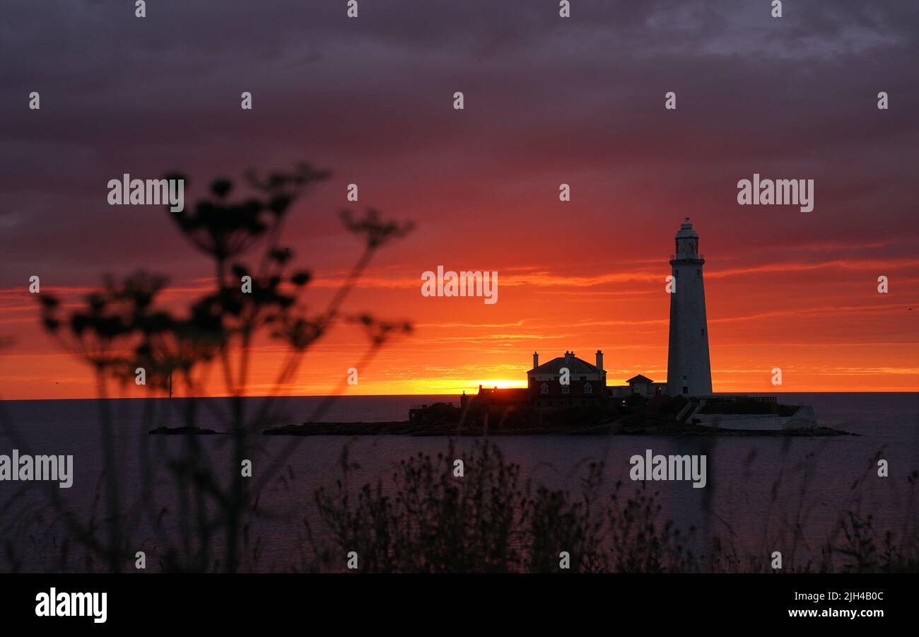 A fire coloured sky above St Mary's Lighthouse in Whitley bay on the North East coast of England just before sunrise. Picture date: Friday July 15, 2022. Stock Photo