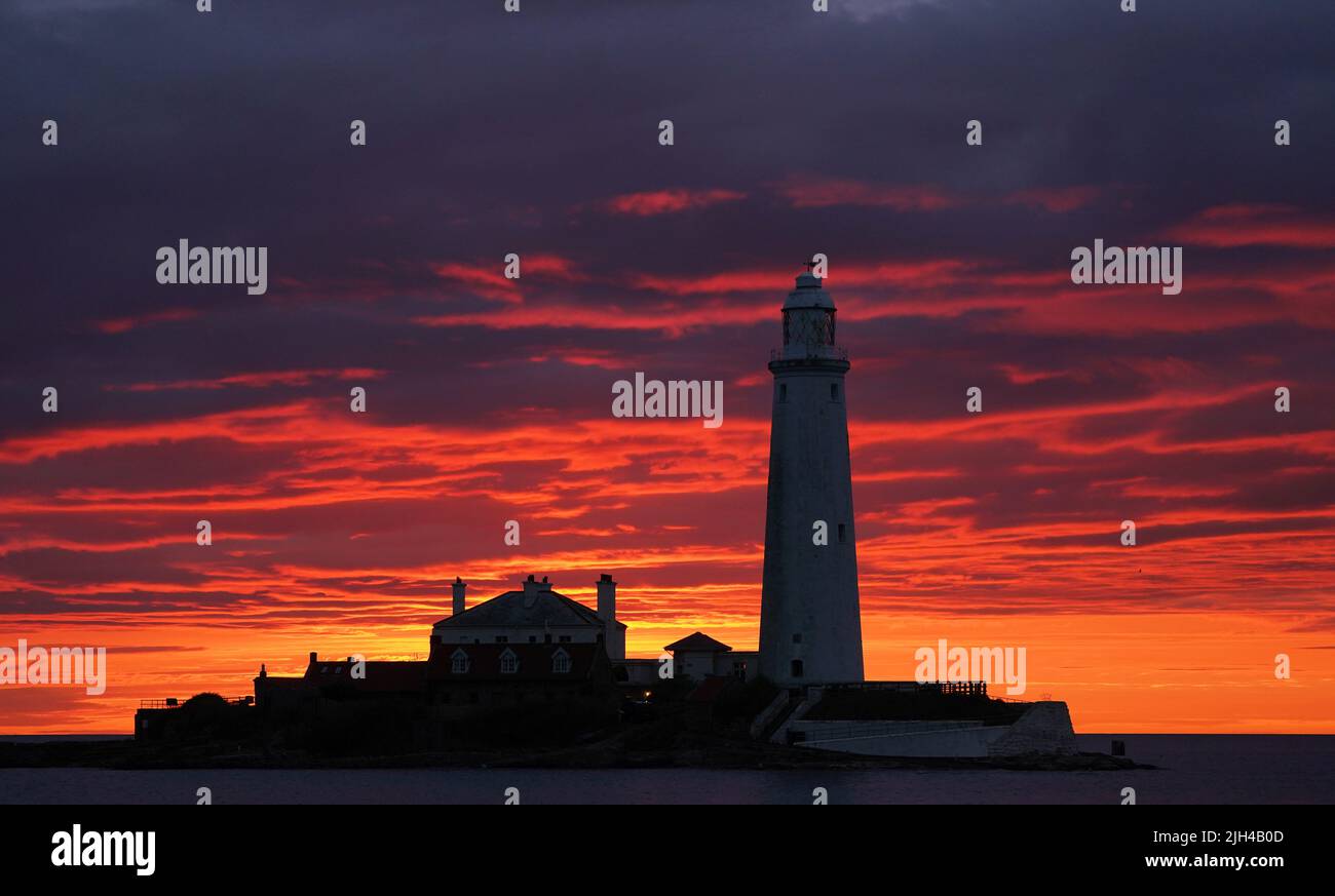A fire coloured sky above St Mary's Lighthouse in Whitley bay on the North East coast of England just before sunrise. Picture date: Friday July 15, 2022. Stock Photo