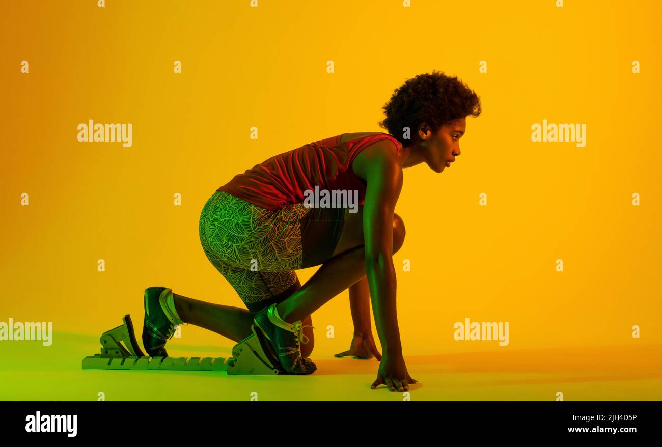 Image of african american female athlete preparing for run in yellow lighting Stock Photo