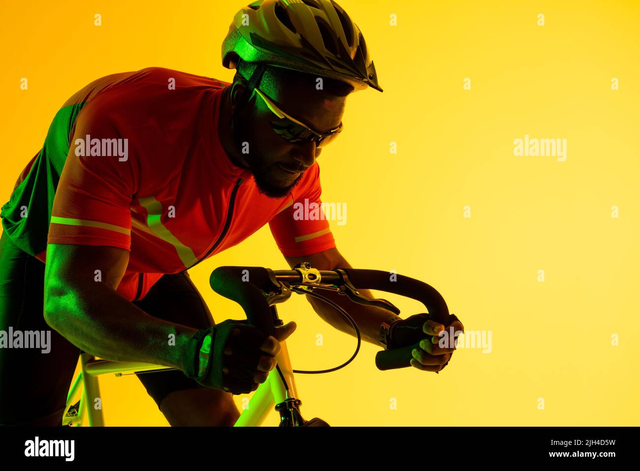 Image of african american male cyclist riding bike in yellow lighting Stock Photo