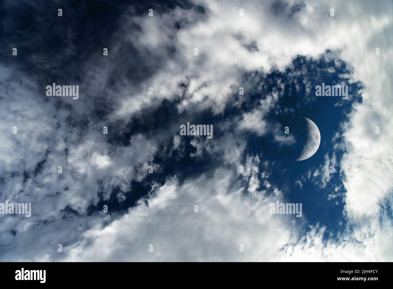 Dark blue dramatic sky background with white clouds and moon. Beautiful atmospheric cloud scape. Cumulus clouds Stock Photo