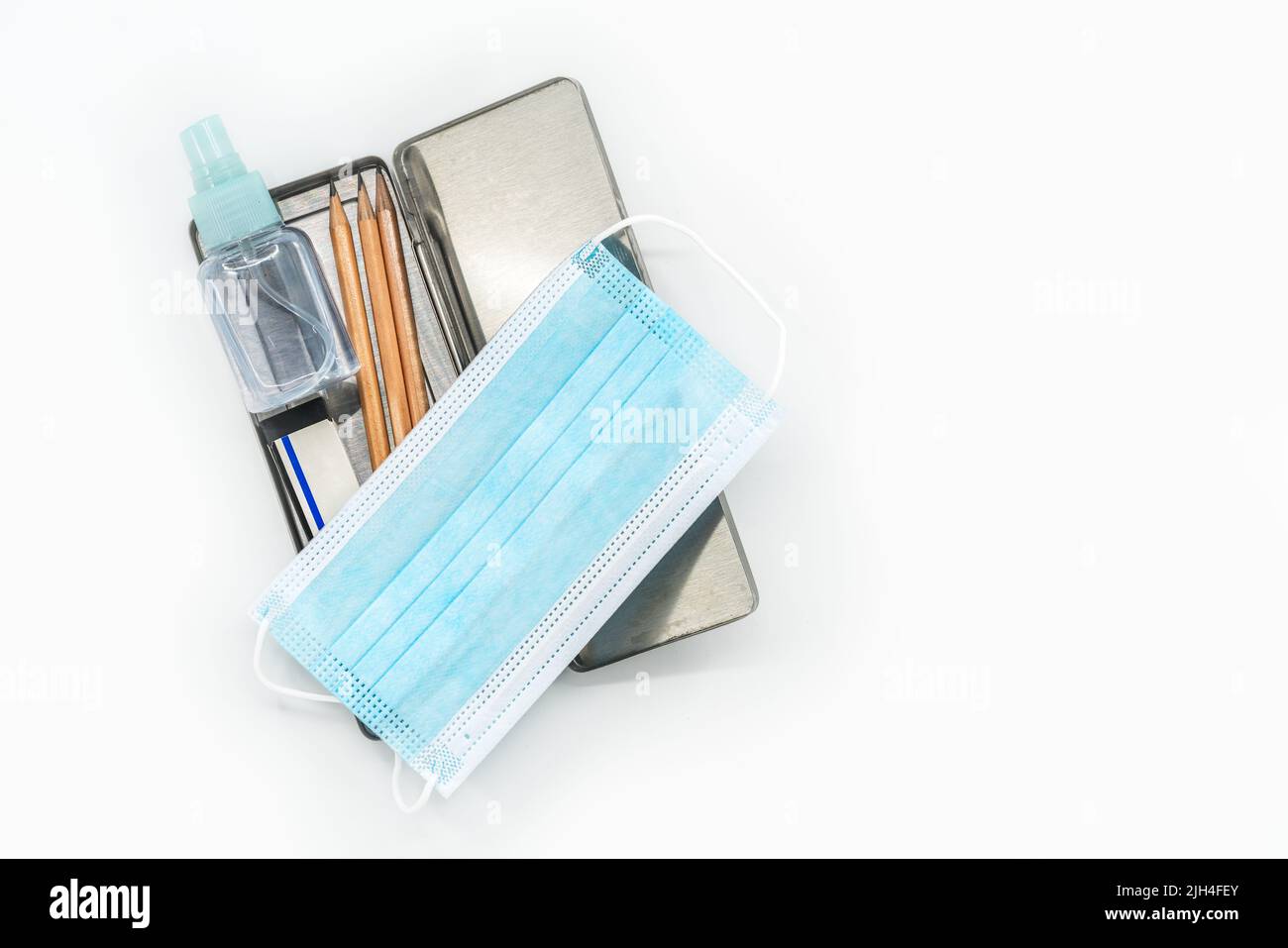 Top view stainless steel pencil box with pencils, medical face mask and a small bottle of alcohol, the isolated image on white background, the concept Stock Photo