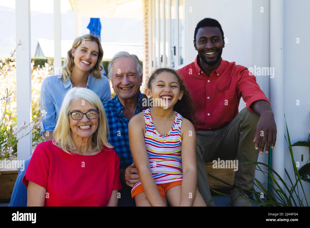 Portrait of cheerful multiracial multigeneration family sitting outside house in yard Stock Photo