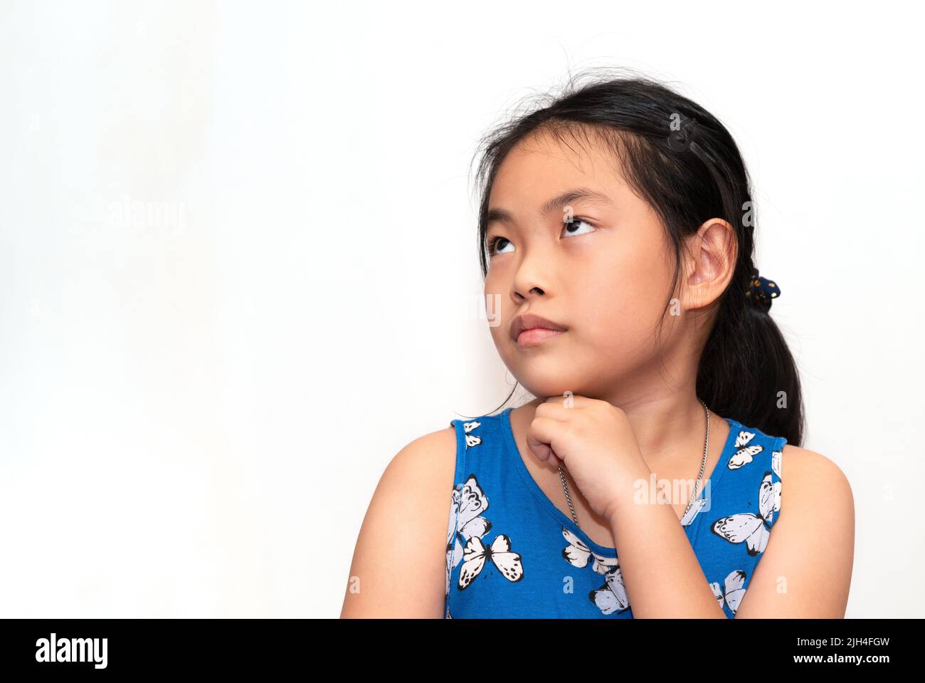 Portrait of cute Asian child girl is thinking, looking at the right side and slightly up, one hand at chin, black long hair, Asian child girl at 8-9 y Stock Photo