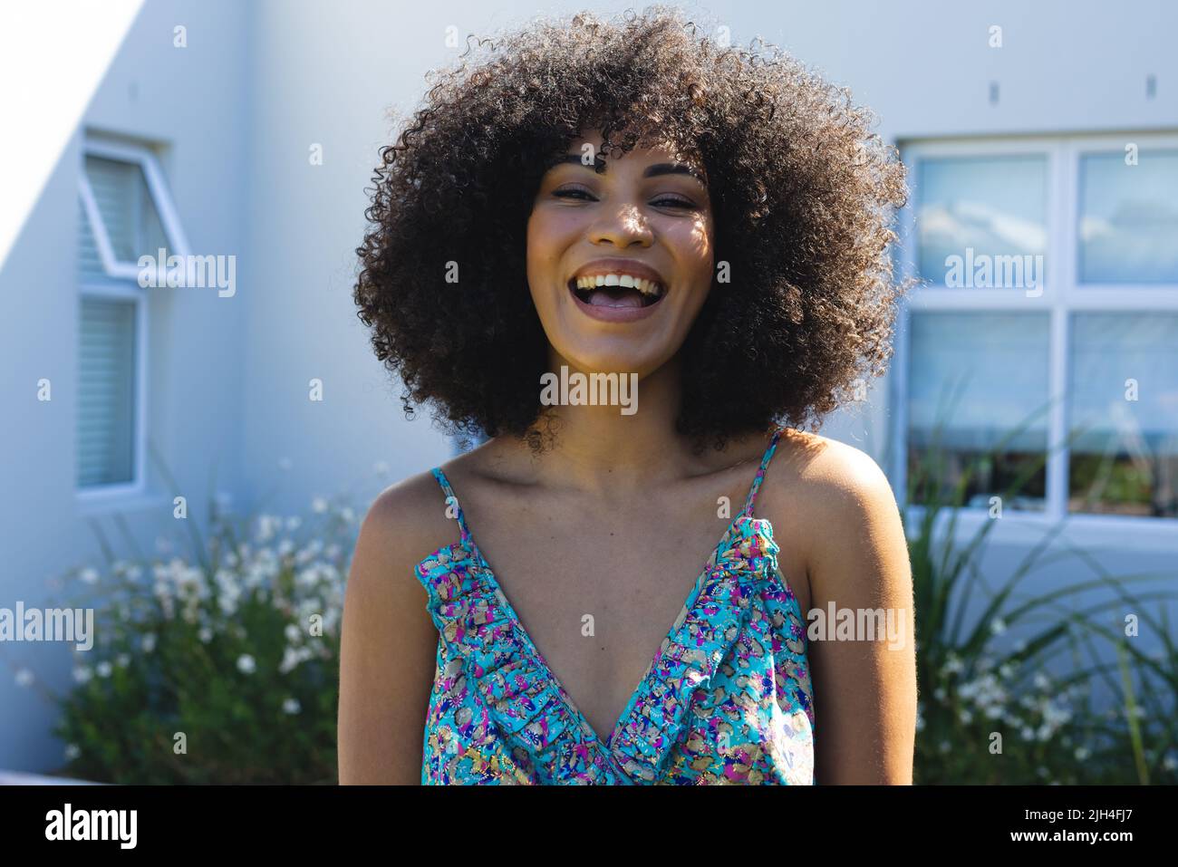 Portrait of biracial beautiful mid adult woman with afro hair laughing against house in yard Stock Photo