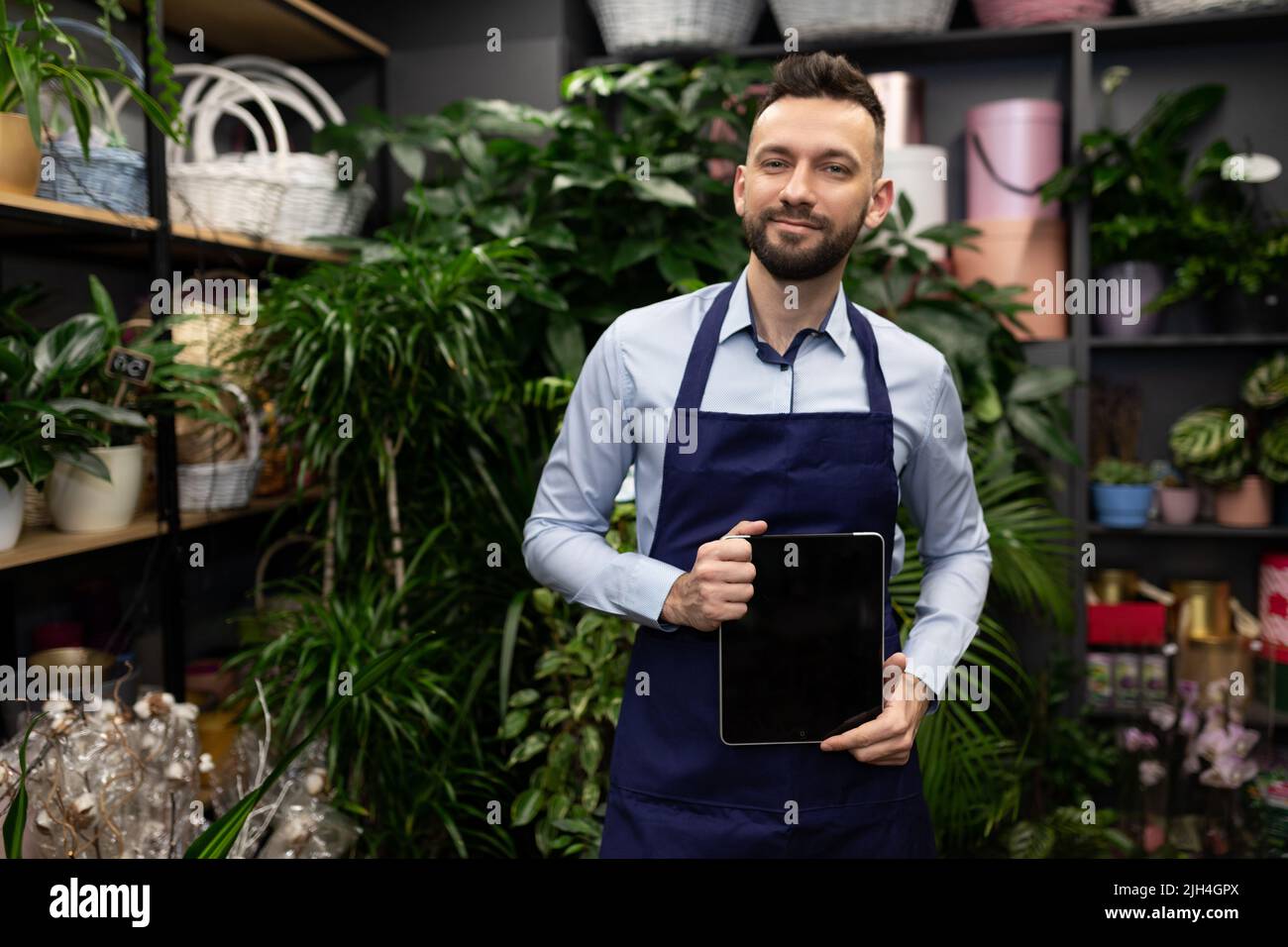 successful flower shop salesman demonstrates tablet screen surrounded