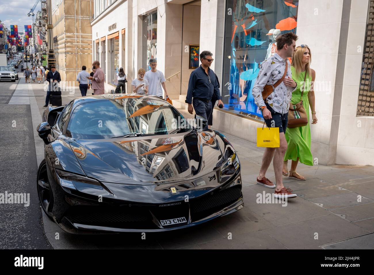 Pedestrian shoppers walk past a shiny Ferrari that has been illegally parked on the narrowed pavement outside Louis Vuitton on New Bond Street, on 14th July, in London, England. Stock Photo