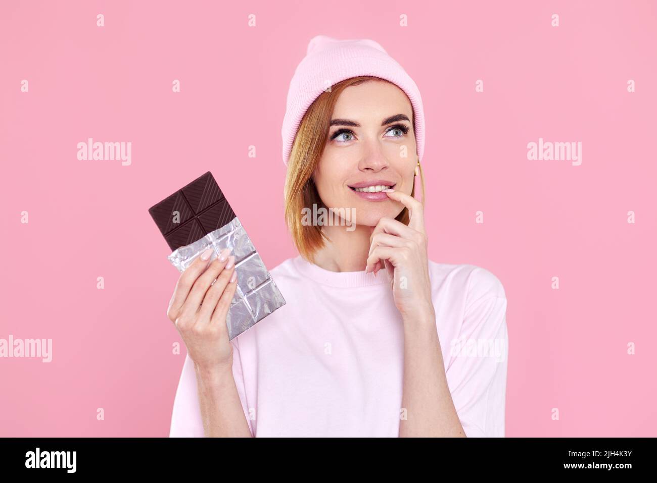 blonde woman in t-shirt and hat holding chocolate bar Stock Photo