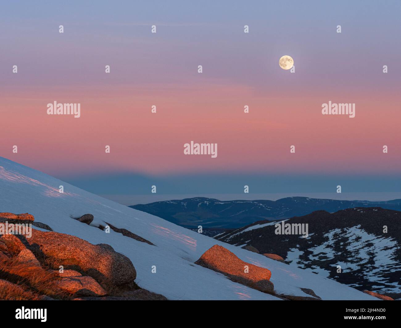 Cairngorms at sunset with colorful Belt of Venus and the rising moon in the sky during the winter season viewed from slopes of Carn Gorm Stock Photo