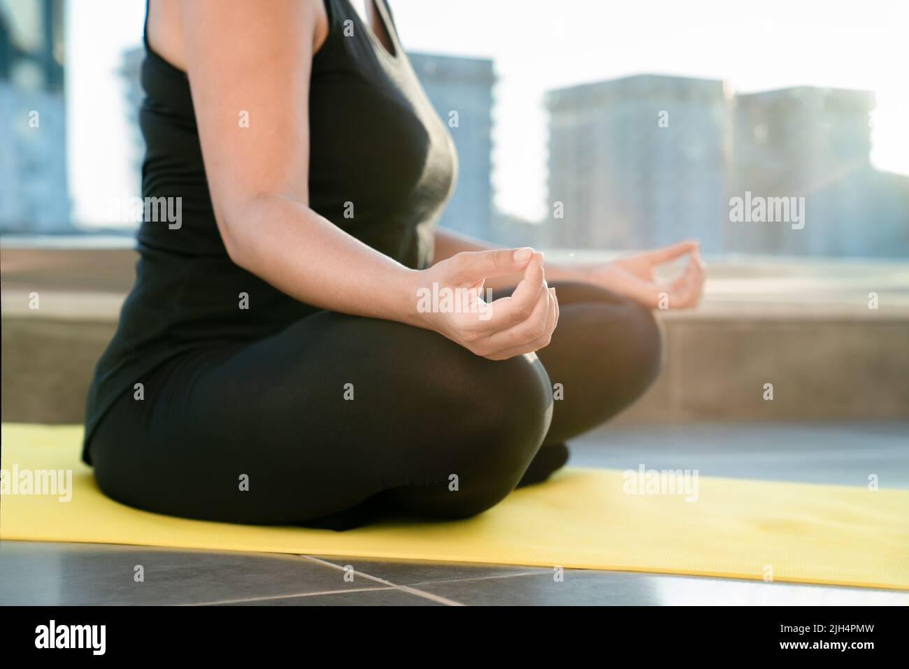 Young woman meditating in lotus position sitting on fitness mat on balcony of her house, close-up. Concept of healthy and harmonious life Stock Photo