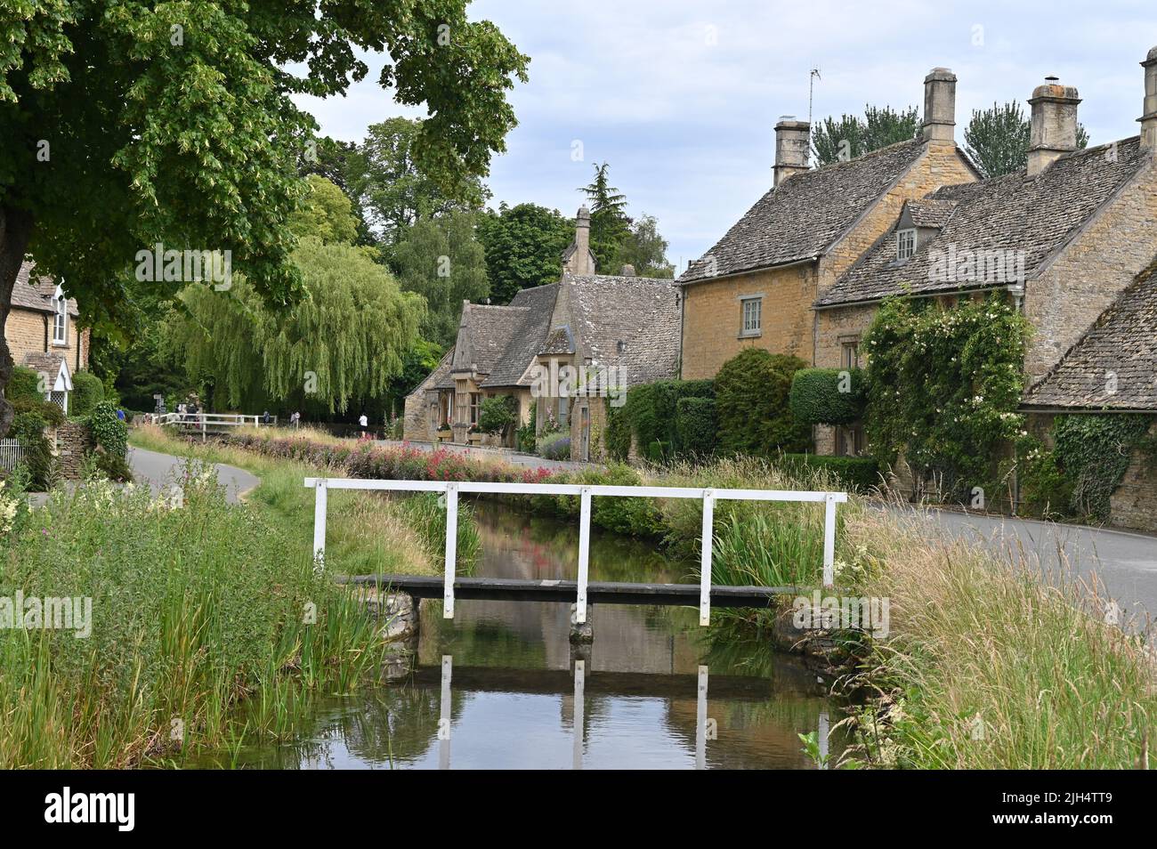 The River Eye flows through the Gloucestershire village of Lower Slaughter with attractive old Cotswold stone buildings in the background Stock Photo