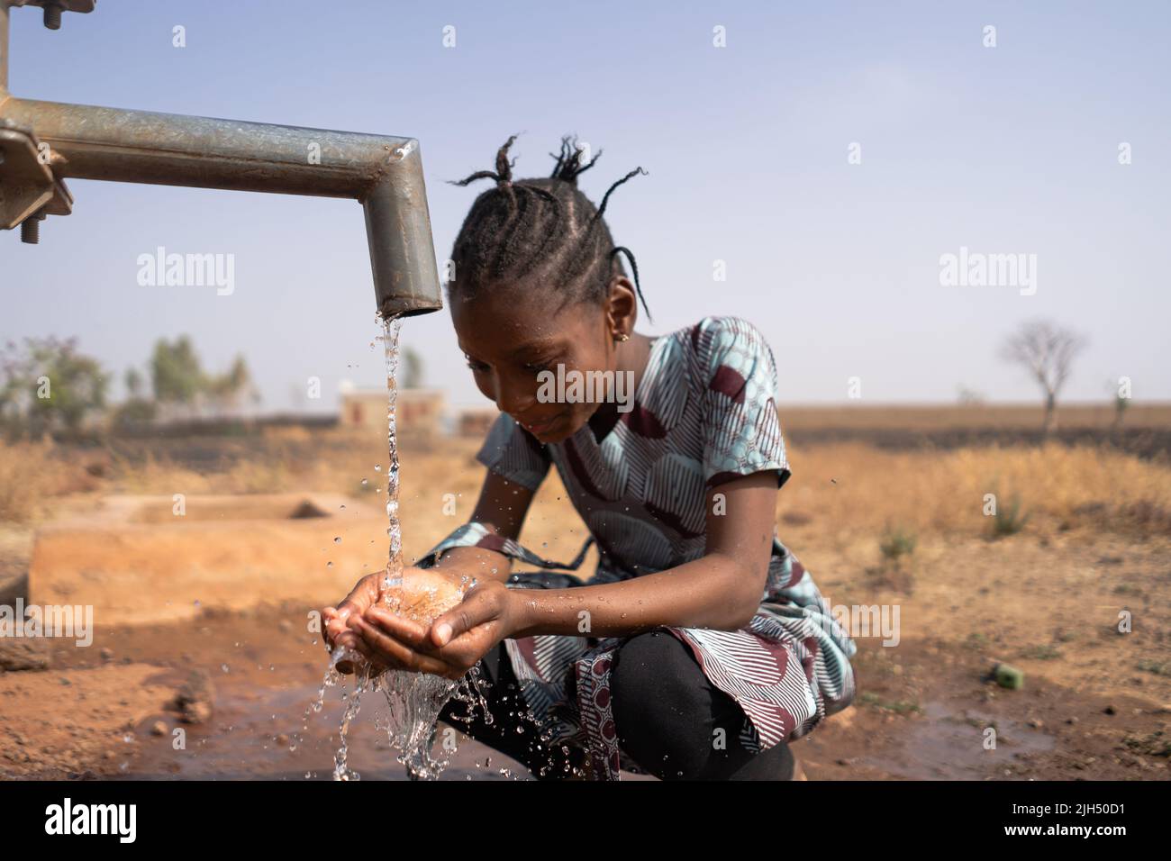 Young African girl happily looking at her handful of water flowing from the village well after a long dry season Stock Photo