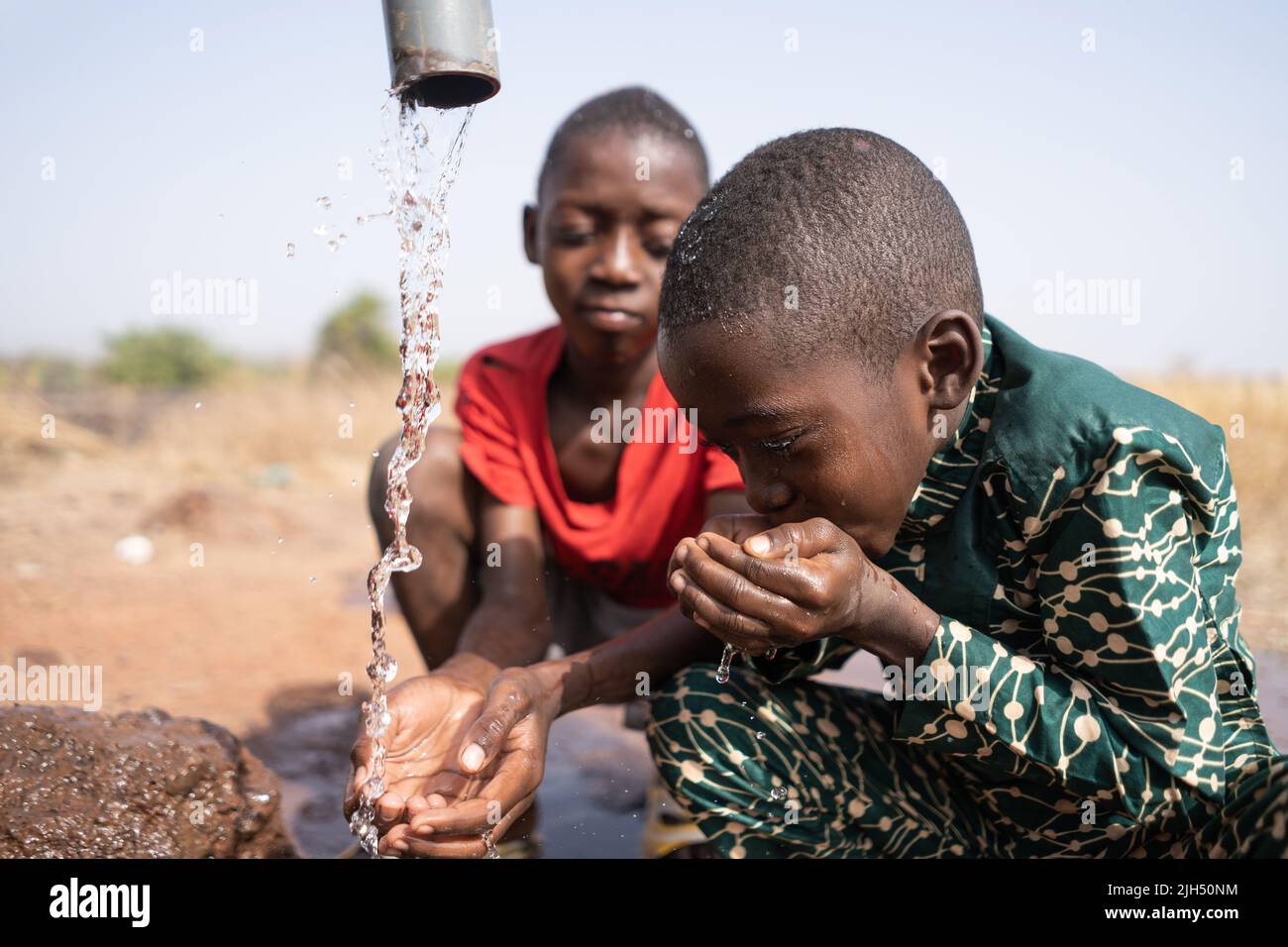 Two little african boys refresh themselves at the village fountain on a sizzling hot day Stock Photo