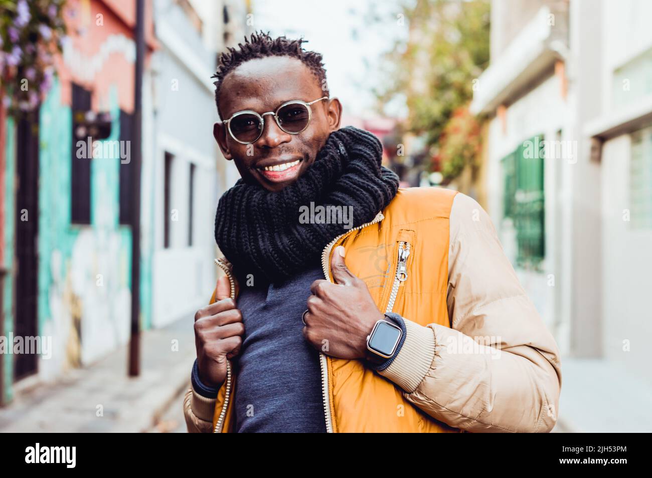 waist up portrait of young black african man, wearing glasses and snorting, smiling and grabbing his jacket lapel, standing in the middle of the stree Stock Photo