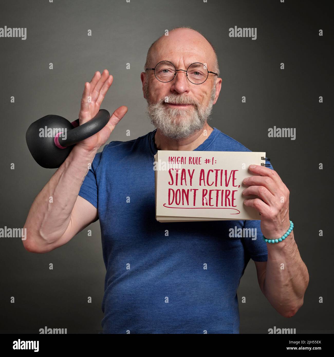 stay active, don't retire, ikigai rule - senior man (in late 60s) with iron kettlebell is holding inspirational note, aging and healthy lifestyle conc Stock Photo