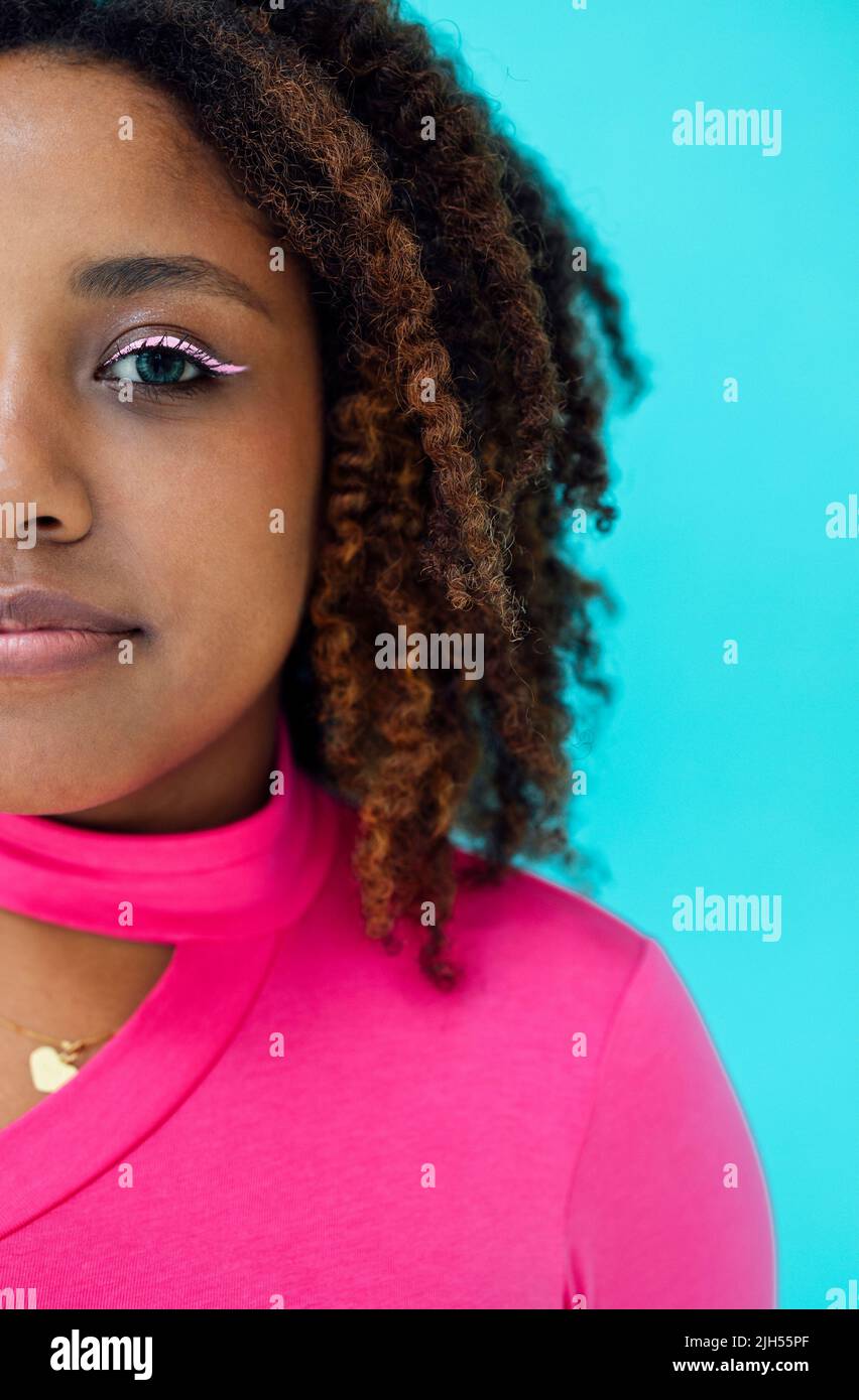 Dreamy young beautiful African American woman with bright eyeline wearing pink bodysuit over blue wall, looks with happy expression Stock Photo