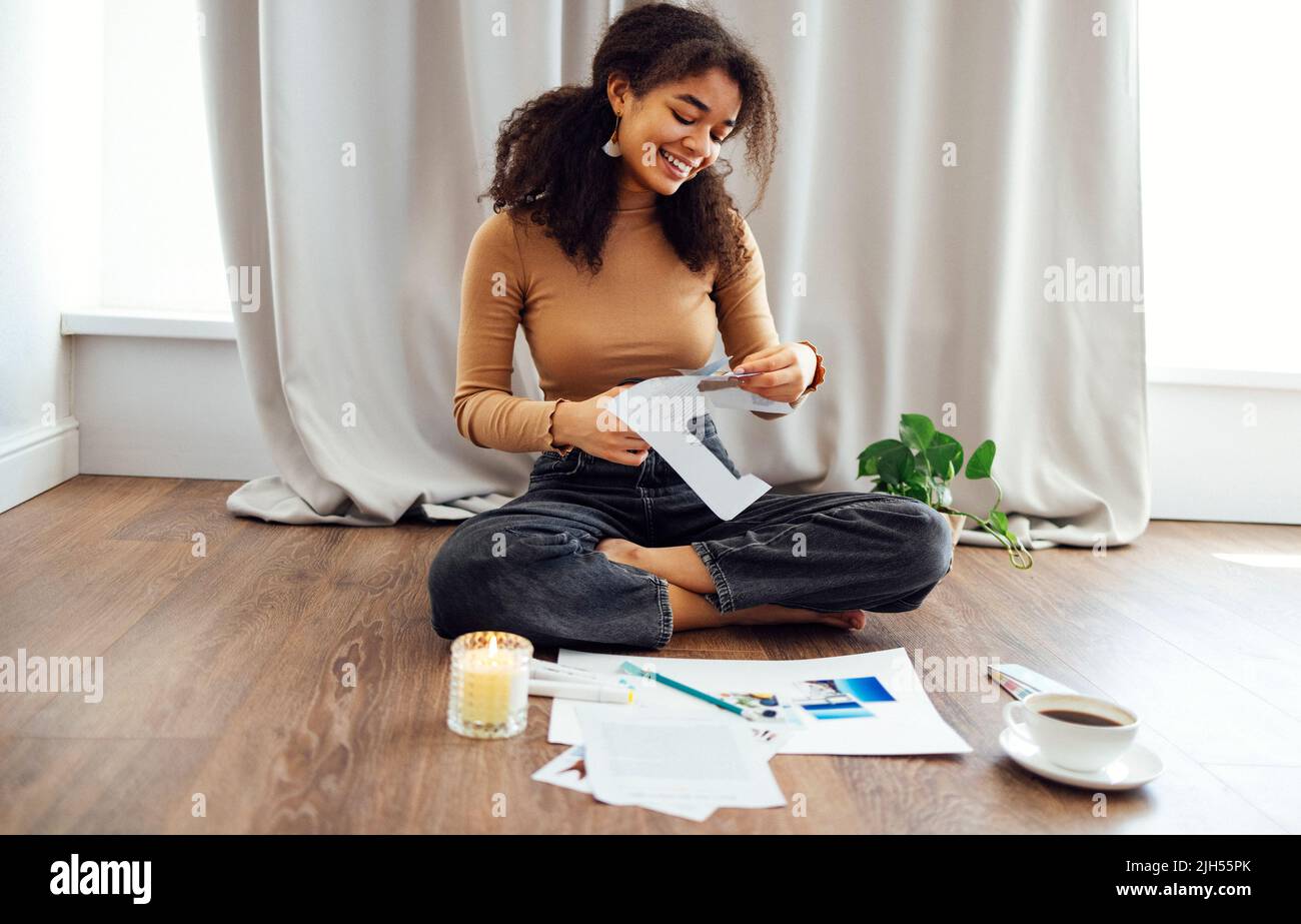 Young brunette african american woman creating her Feng Shui wish map using scissors. Dreams and wishes Stock Photo