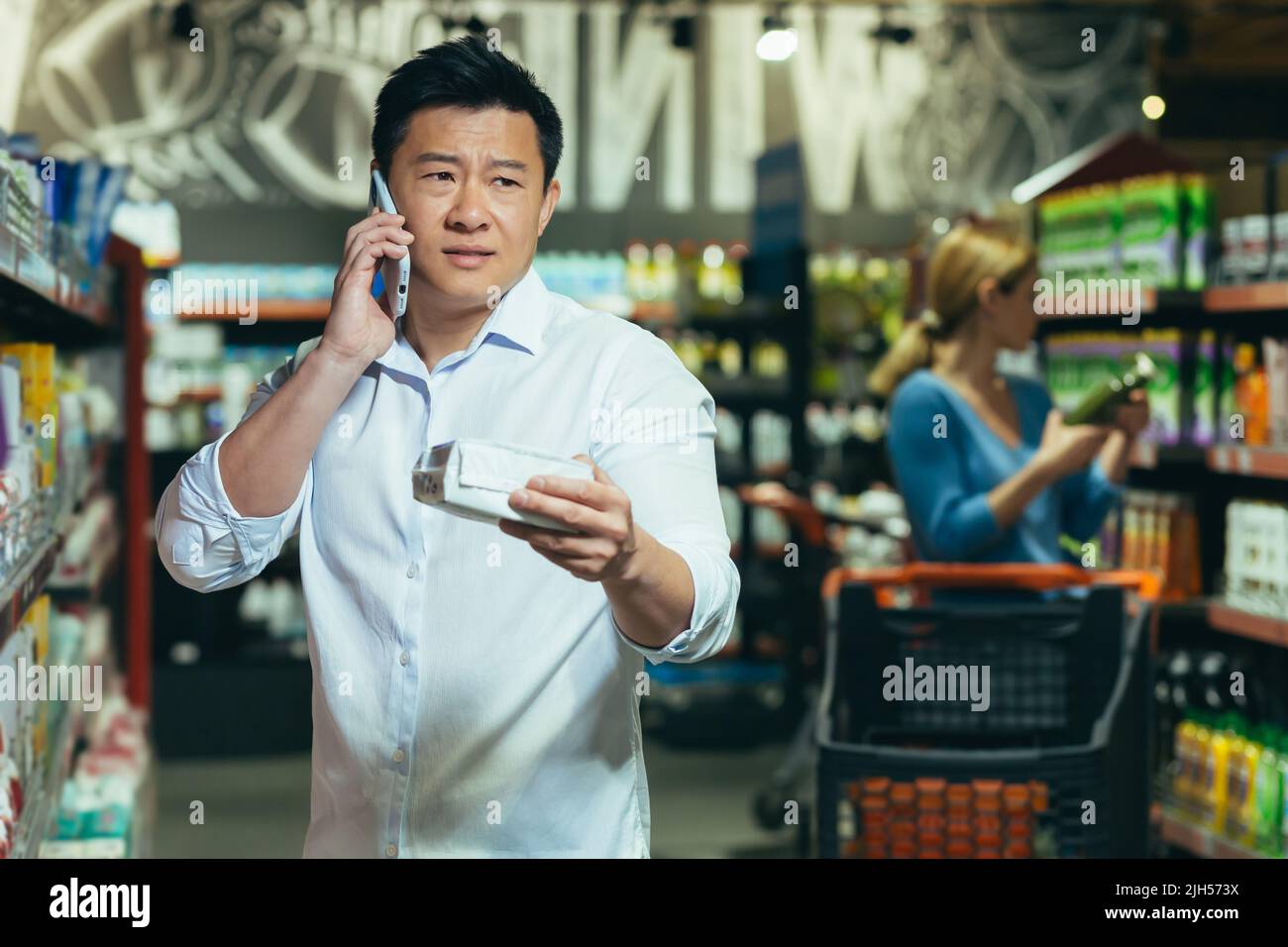 An Asian man cannot choose a product in a supermarket, has difficulty ...