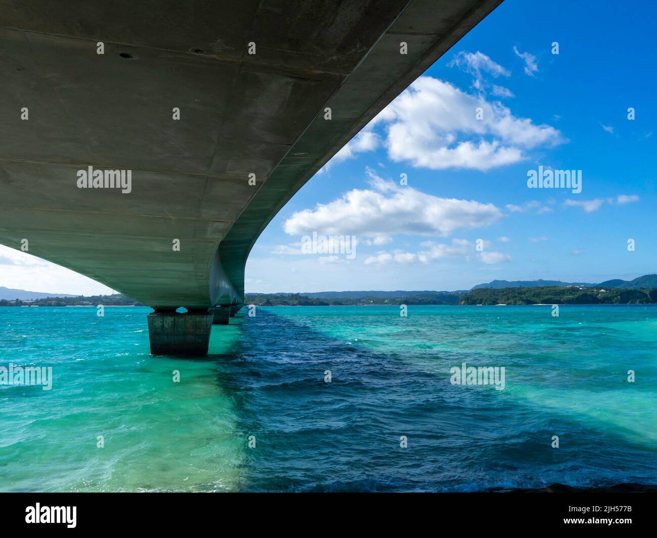 Kouri Bridge in Okinawa against blue sky and white clouds. Green and blue ocean on the bottom. Stock Photo