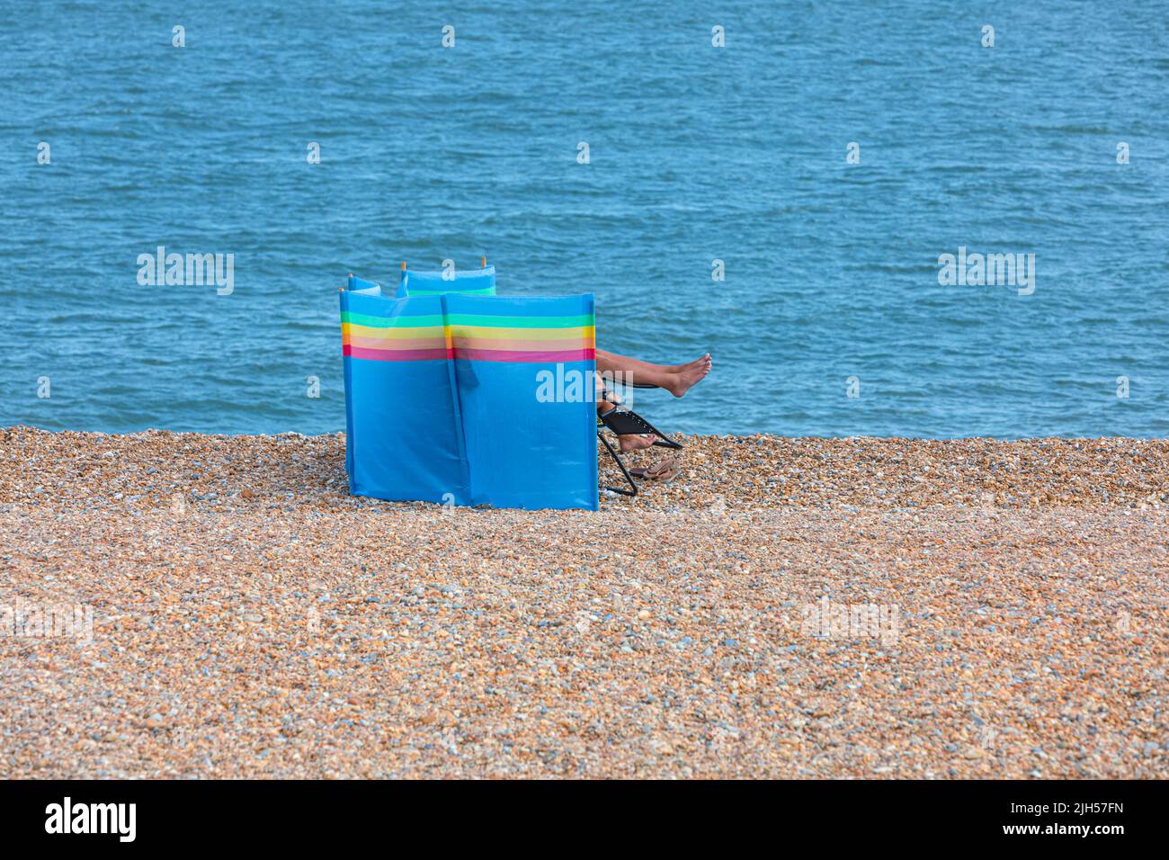 A couple relaxing on a shingle beach with a windbreak Stock Photo