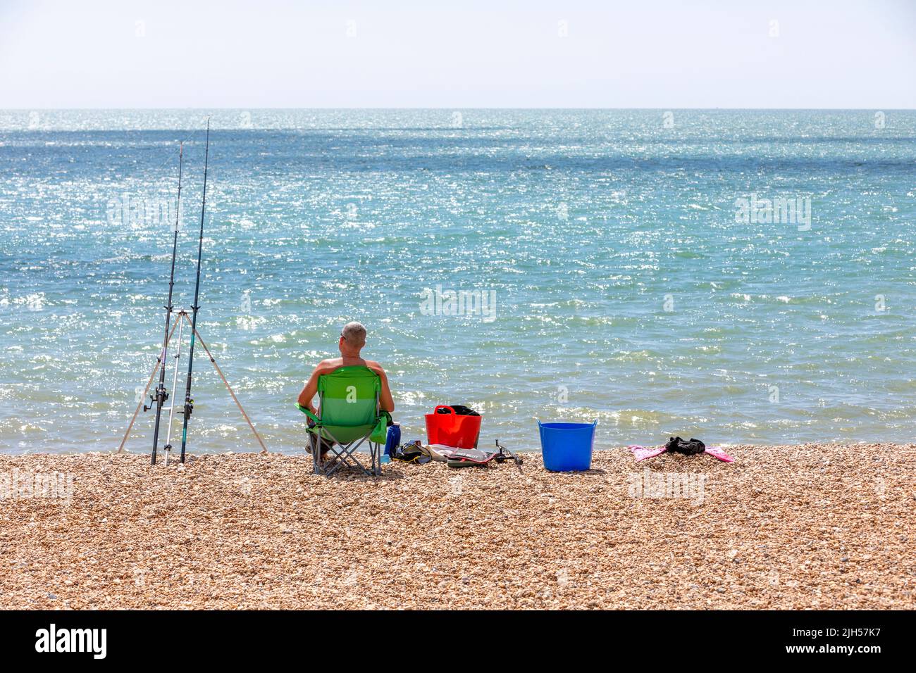 A fisherman sat in a chair on a shingle beach Stock Photo