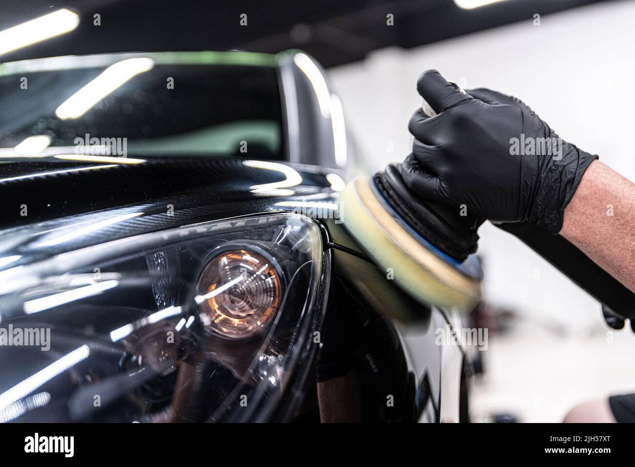 Employee of a car wash or a car detailing studio polishes the car paint