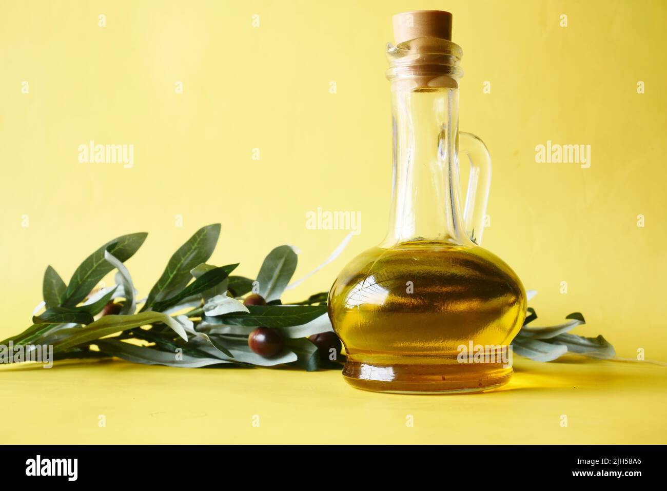 bottle of olive oil and fresh olive with leaf in a container on yellow